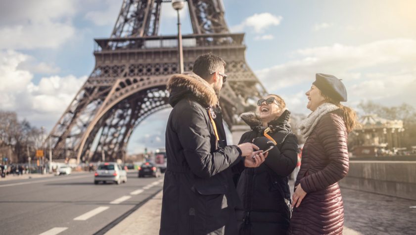 Grupo de amigos conversando y riendo en francés junto a la torre Eiffel