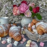 Dulces y croissants sobre una mesa con flores y "chuches", placeres culpables.