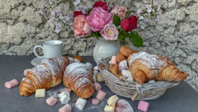 Dulces y croissants sobre una mesa con flores y "chuches", placeres culpables.