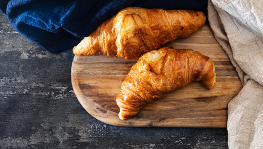Unos deliciosos croissants en una tabla de madera, sobre una mesa lista para desayuno