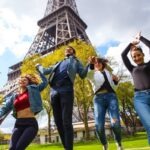 Grupo de chicos jóvenes de viaje por Francia, junto a la torre Eiffel, saltando para la foto