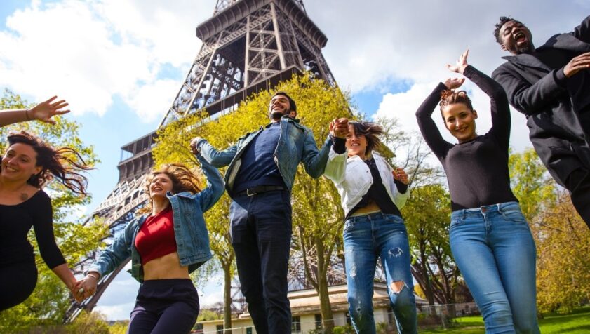 Grupo de chicos jóvenes de viaje por Francia, junto a la torre Eiffel, saltando para la foto